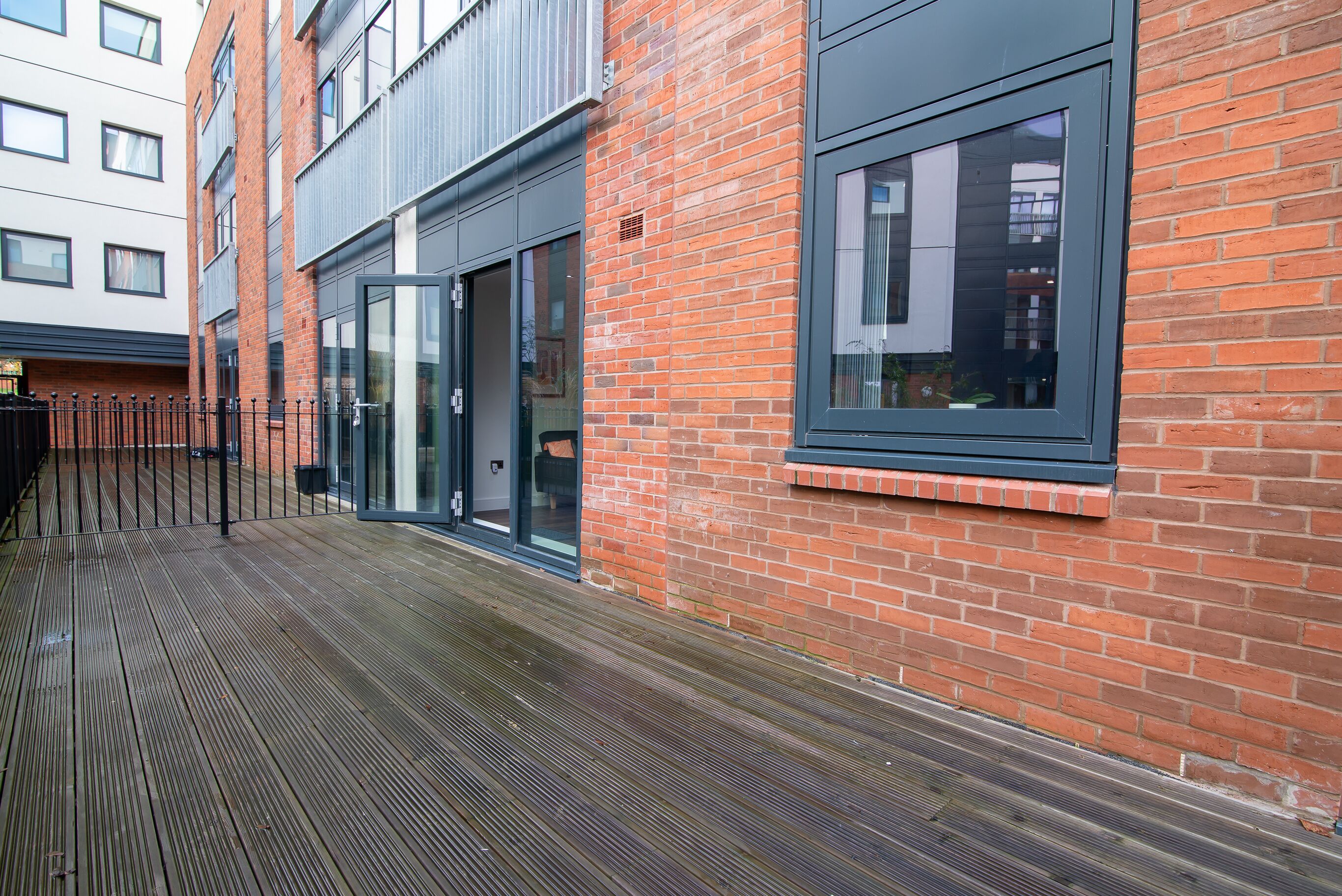 Een modern gebouw met een bakstenen gevel, grote ramen en een houten terras.