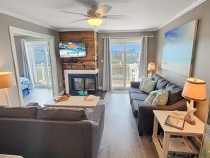 Ein Wohnzimmer mit Kamin, Deckenventilator und Fernseher, der 'OCMD GETAWAYS' anzeigt.