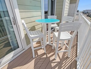 Un balcon avec une table ronde et quatre chaises blanches, une porte vitrée et une vue sur la rue.