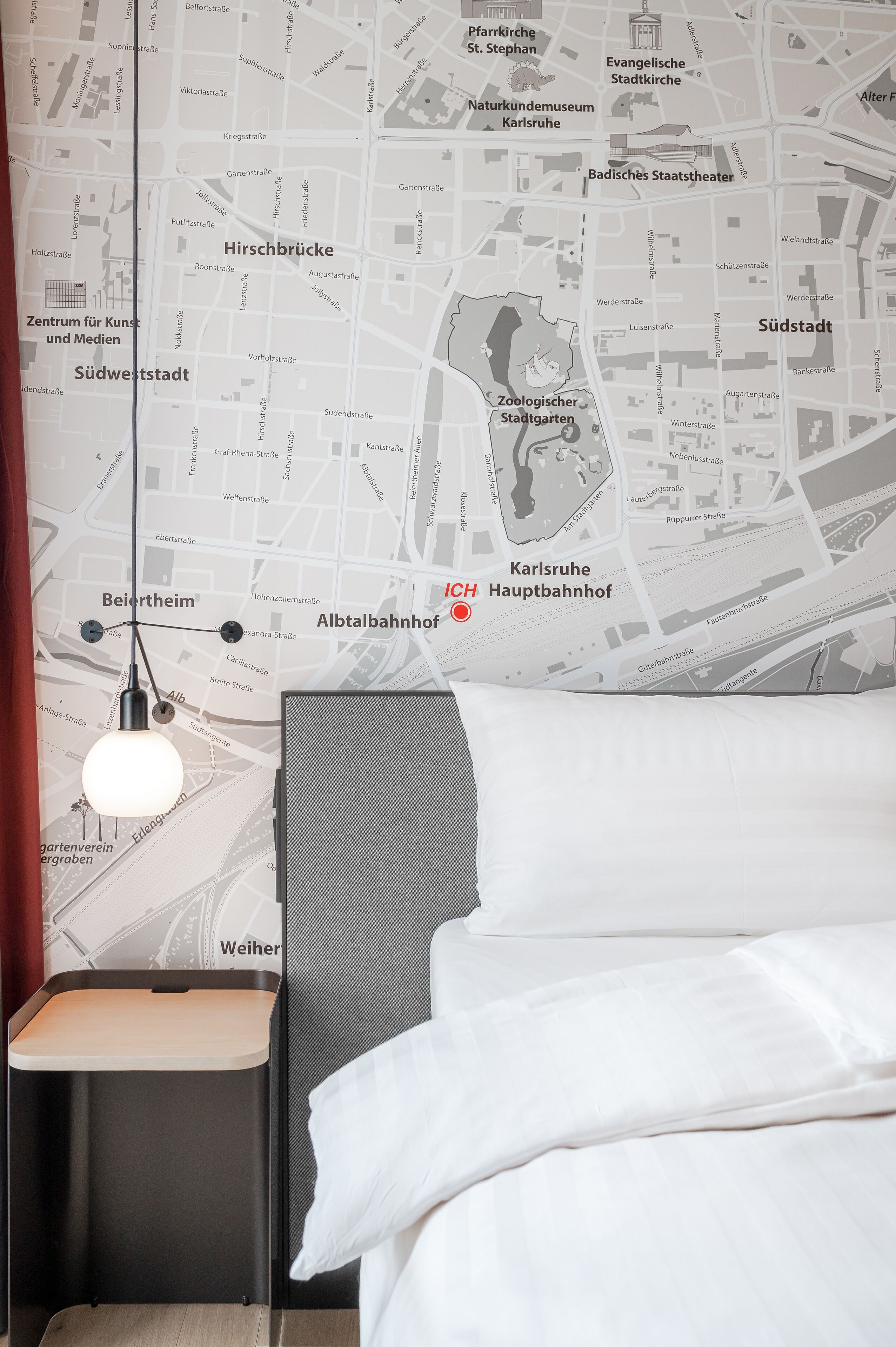 A hotel room with a map wall, a bed, a nightstand, and a hanging light fixture.