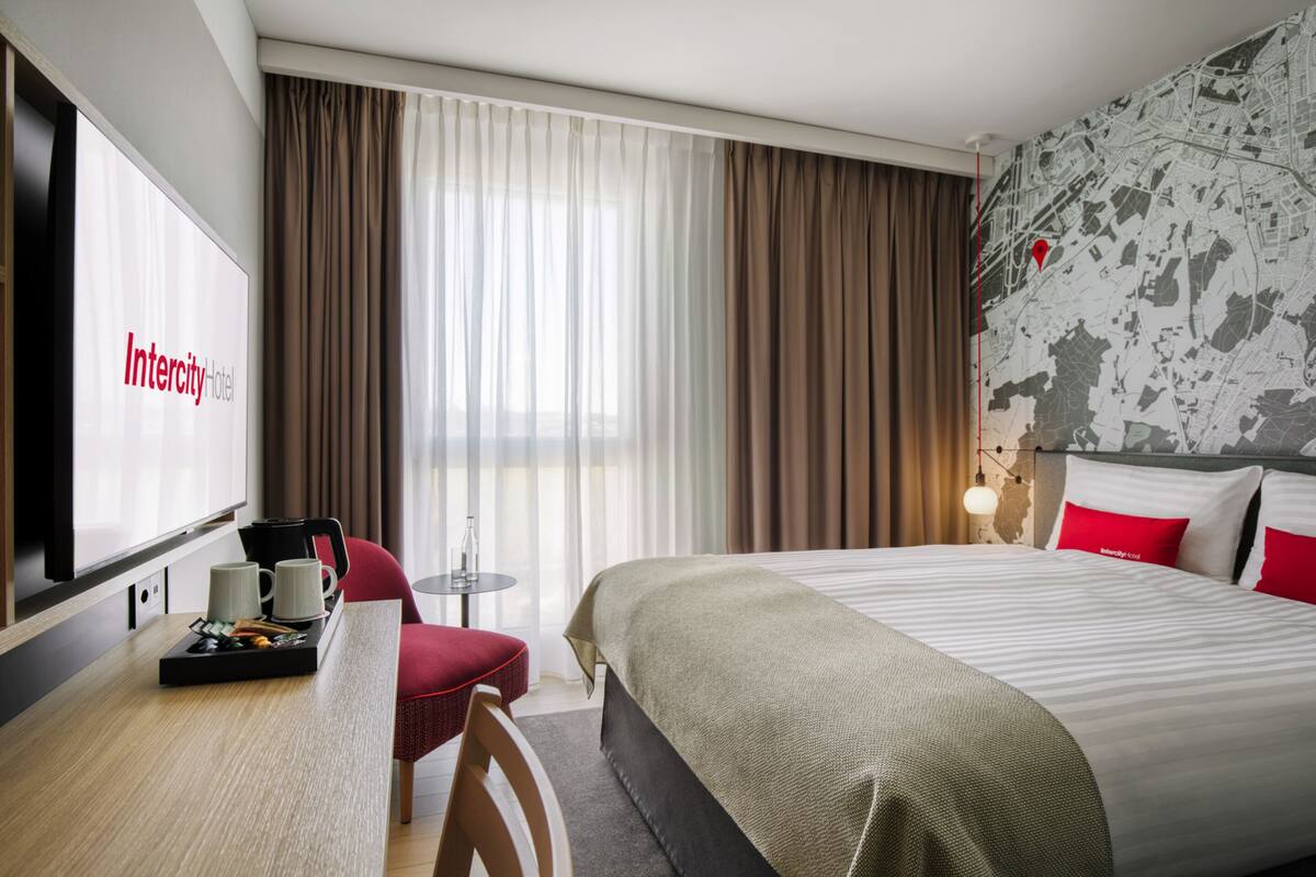 A hotel room with a bed, a desk with a coffee maker, a chair, a TV, and curtains.