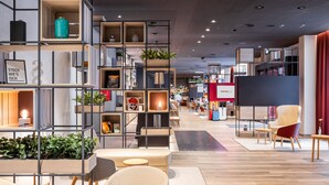 A modern hotel lobby with open shelving, seating areas, and a central red accent wall. - IntercityHotel Karlsruhe (Karlsruhe)