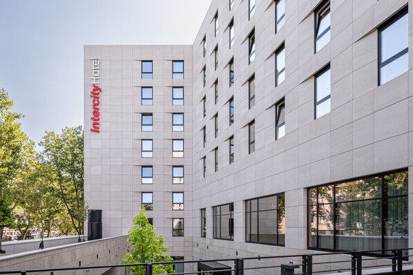 Un edificio moderno con un letrero que dice "Intercity Hotel". Presenta una cuadrícula de ventanas y una fachada plana.