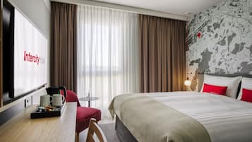 Habitación de hotel con cama, escritorio con cafetera, silla, televisor y cortinas.