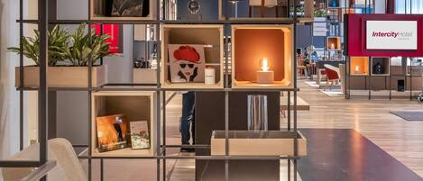 Un moderno vestíbulo de hotel con un área de descanso central, una estantería escalonada con plantas y objetos decorativos, y un letrero del Hotel Intercity.