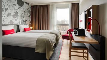 Habitación de hotel con una cama grande, un escritorio con computadora, televisor y ventana con cortinas.