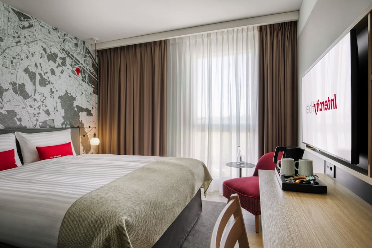 A hotel room with a large bed, a desk with a chair, a small table, and a TV.