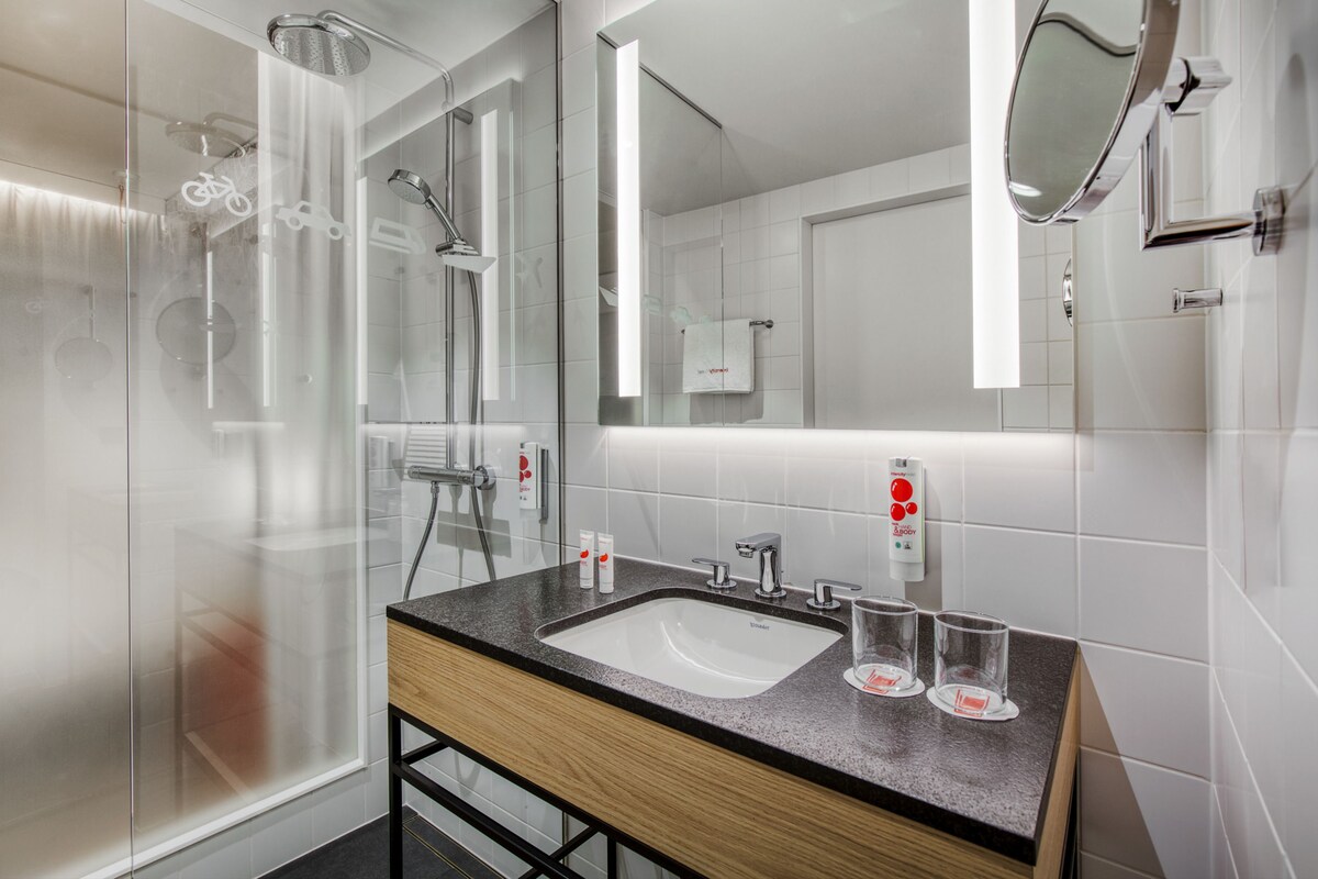 A modern bathroom with a glass shower enclosure, a wooden vanity with a sink, and a large mirror.