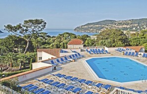A pool area with multiple lounge chairs and a large pool, surrounded by greenery and overlooking a coastal landscape.
