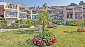 Un hotel de diverses plantes amb balcons, un jardí ben cuidat i un cel serè.