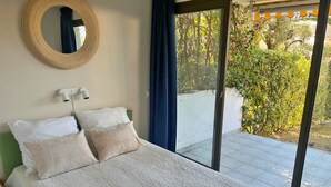 Un dormitori amb un llit, un mirall rodó i vista a un jardí per una porta corredissa de vidre.