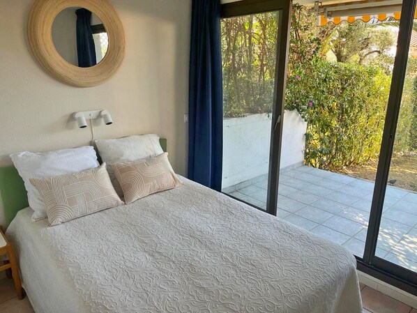 A bedroom with a bed, a round mirror, and a view of a garden through a sliding glass door.