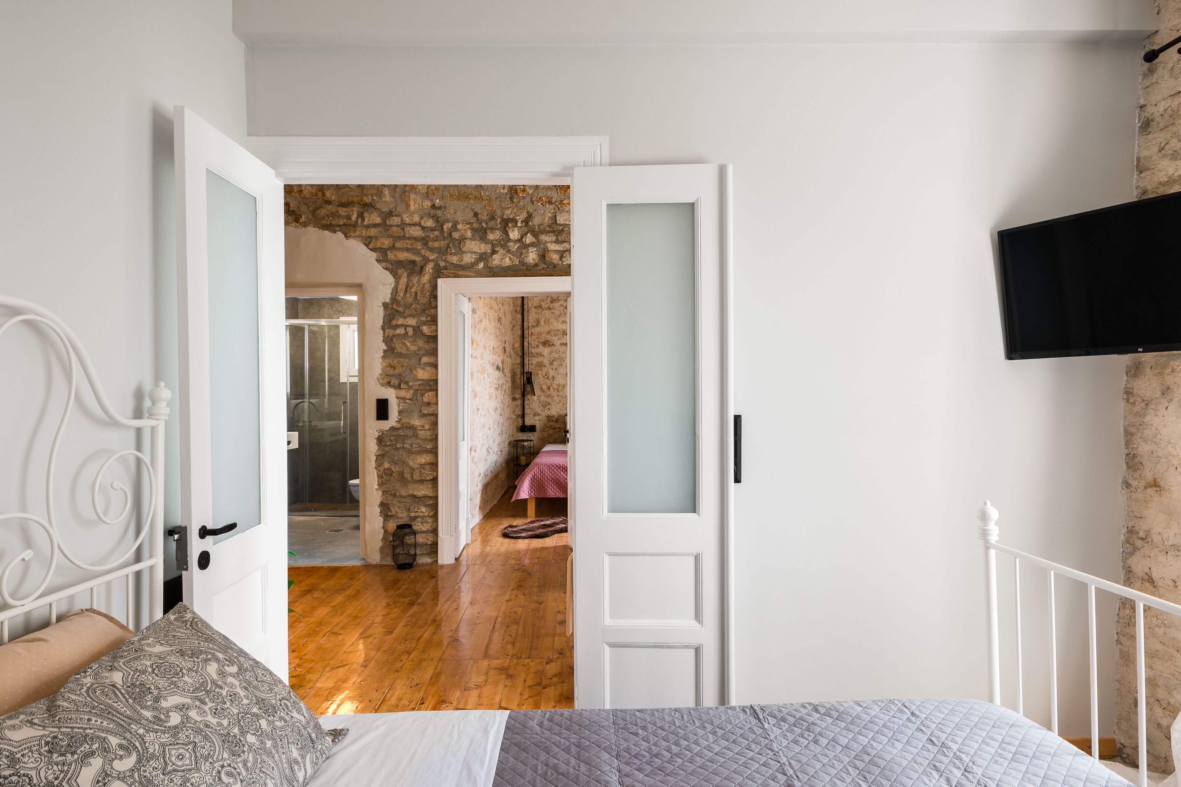 A bedroom with a bed, a TV mounted on the wall, and a stone wall in the background.