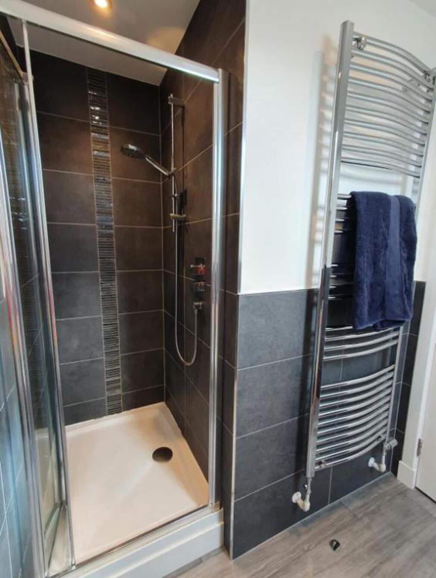 A walk-in shower with a glass door, a towel rack with a blue towel, and a metal towel rack.