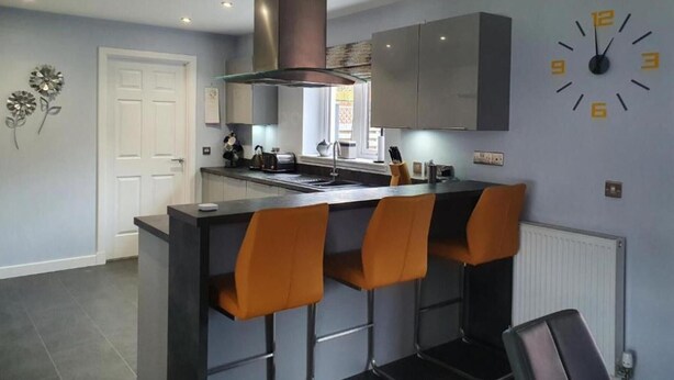 Una cocina moderna con una isla central, taburetes de bar y un reloj en la pared.