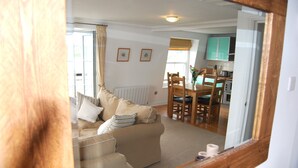 A cozy living room with a sofa, a dining table with chairs, and a kitchen area in the background. - Crows Nest: a modern apartment in the centre of St Mawes with stunning sea views (St Mawes)