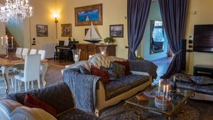 A well-furnished living room with a sofa, chairs, a dining table, and a chandelier. - Magnificent Luxury Villa in Rome. Private pool and large garden. (Roma)