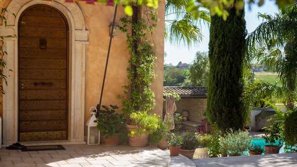 A stone entrance with a wooden door, potted plants, and a tiled patio area. - Magnificent Luxury Villa in Rome. Private pool and large garden. (Roma)