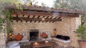 A stone-walled outdoor seating area with a fireplace, wooden benches, and a coffee table. - Magnificent Luxury Villa in Rome. Private pool and large garden. (Roma)