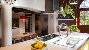A modern kitchen with a central island, a gas stove, and a sink. There is a dining area with a table and chairs, and a red pendant light above the island. - Magnificent Luxury Villa in Rome. Private pool and large garden. (Roma)