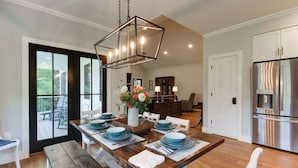 A modern kitchen with a stainless steel refrigerator, wooden dining table set with blue plates, and a hanging light fixture. - Bellview Cottage - MOUNTAIN HOUSE VACATION RENTAL (Hot Springs)