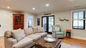 A living room with a beige sofa, a brown ottoman, a light blue armchair, and a wooden cabinet. - Bellview Cottage - MOUNTAIN HOUSE VACATION RENTAL (Hot Springs)