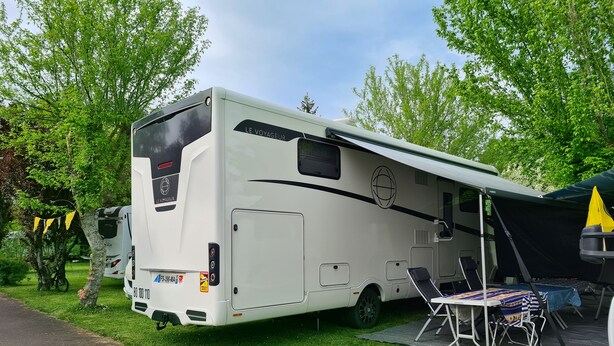 A white RV with a side entrance and a covered area with a table and chairs. - Electrified Camping Pitch (Bessé-sur-Braye)
