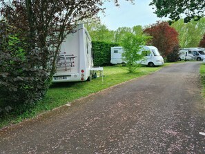 Ein Campingplatz mit Reisemobilen, die an einem befestigten Weg entlang geparkt sind, umgeben von Grün.