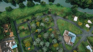 Vue aérienne d’un quartier résidentiel avec une rivière, des pelouses verdoyantes, des arbres et quelques bâtiments, dont une maison avec un toit bleu et une structure moderne dotée d’une façade en verre.