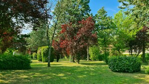 A well-maintained garden with various trees and shrubs, a clear sky, and a pathway. - Electrified Camping Pitch (Bessé-sur-Braye)