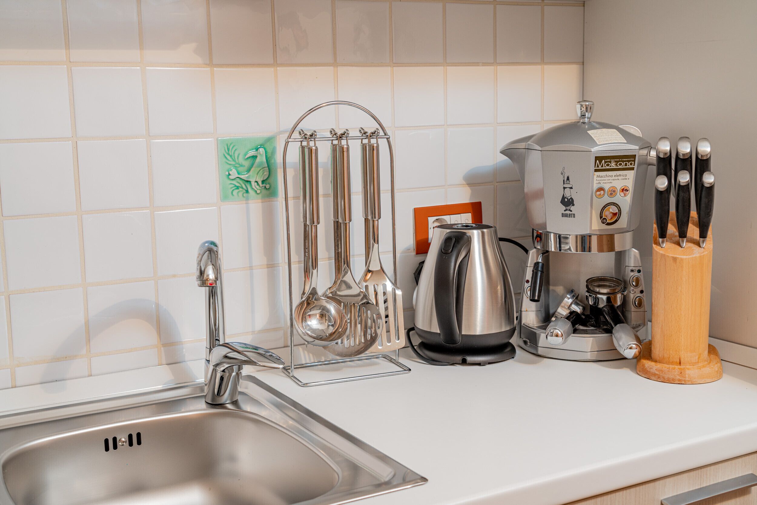 A kitchen counter with a stainless steel sink, a coffee maker, a kettle, and a knife block.