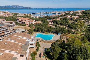An aerial view of a coastal residential area with a large swimming pool surrounded by houses and greenery.