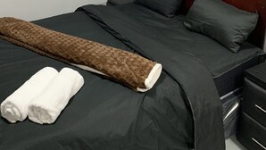 Una cama bien tendida con una colcha oscura y almohadas, una manta marrón y dos toallas blancas sobre la cama.