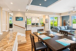 A modern interior with a dining area, kitchen, and living room, featuring a staircase and large windows. - Elegant Wailea Remodeled 2BR Condo Saltwater Pool Steps to Keawakapu Beach (Wailea)