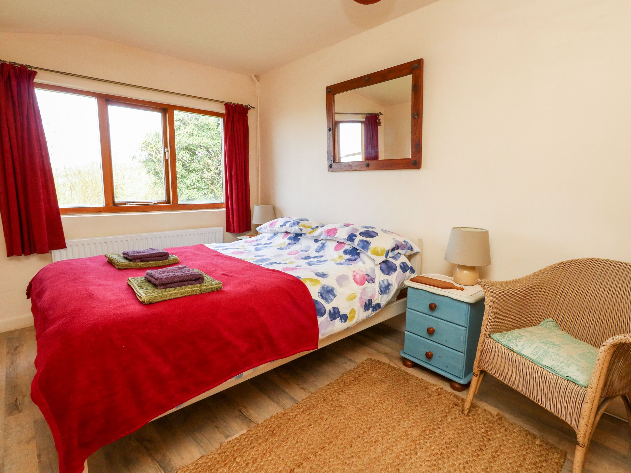 A bedroom with a bed, a nightstand, a chair, a mirror, and a window with curtains.