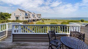 A wooden deck with outdoor furniture, overlooking a beach and a house with multiple levels. - Vacation Rental in the Bayfront Community of Port Lewes (Lewes Beach)