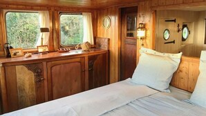 A cabin-style bedroom with a wooden ceiling, a bed with striped bedding, a nightstand, a window with curtains, and a door with a lantern. - Authentic Fisherman’s Cabin • Audierne Bay • Brittany • 2 Guests (Saint-Jean-Trolimon)