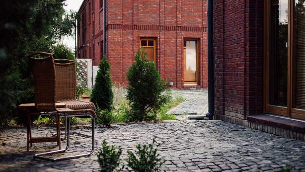 Un patio empedrado con una silla de mimbre y un pequeño árbol.