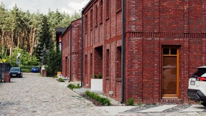 Un edificio de ladrillo rojo con una puerta de madera, coches aparcados y una calle empedrada.