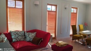 Una sala de estar con un sofá rojo, sillas amarillas, una mesa de vidrio y un comedor.