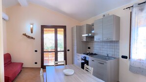 A compact kitchen with a dining table, a red sofa, and a window with curtains. - Villa Patrizia (Castiadas)
