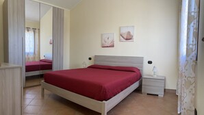 A bedroom with a bed, bedside tables, a mirror, and two wall art pieces. - Villa Patrizia (Castiadas)