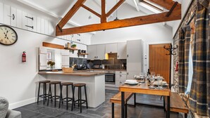 A modern kitchen with dark tiles, wooden beams, and a central island with stools. - Stylish barn nestled in a scenic setting (Laugharne)