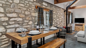 A dining area with a stone wall, wooden table, benches, and a fireplace. - Stylish barn nestled in a scenic setting (Laugharne)