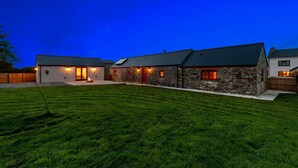 A two-story house with a stone exterior, a green roof, and a well-maintained lawn. - Stylish barn nestled in a scenic setting (Laugharne)
