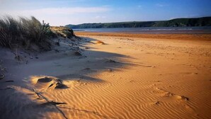 A sandy beach with dunes and a clear sky. - Stylish barn nestled in a scenic setting (Laugharne)