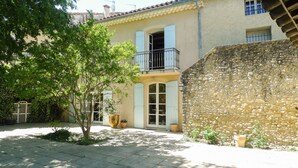 Une cour avec un mur en pierre, un arbre et un bâtiment doté d’un balcon.