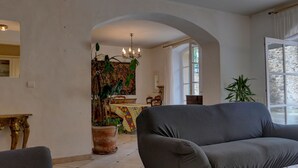Un salon avec un canapé, un coin repas avec une table et des chaises, et une grande fenêtre avec des rideaux.