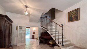 Un hall d’entrée spacieux avec un grand escalier, un meuble en bois et un piano.
