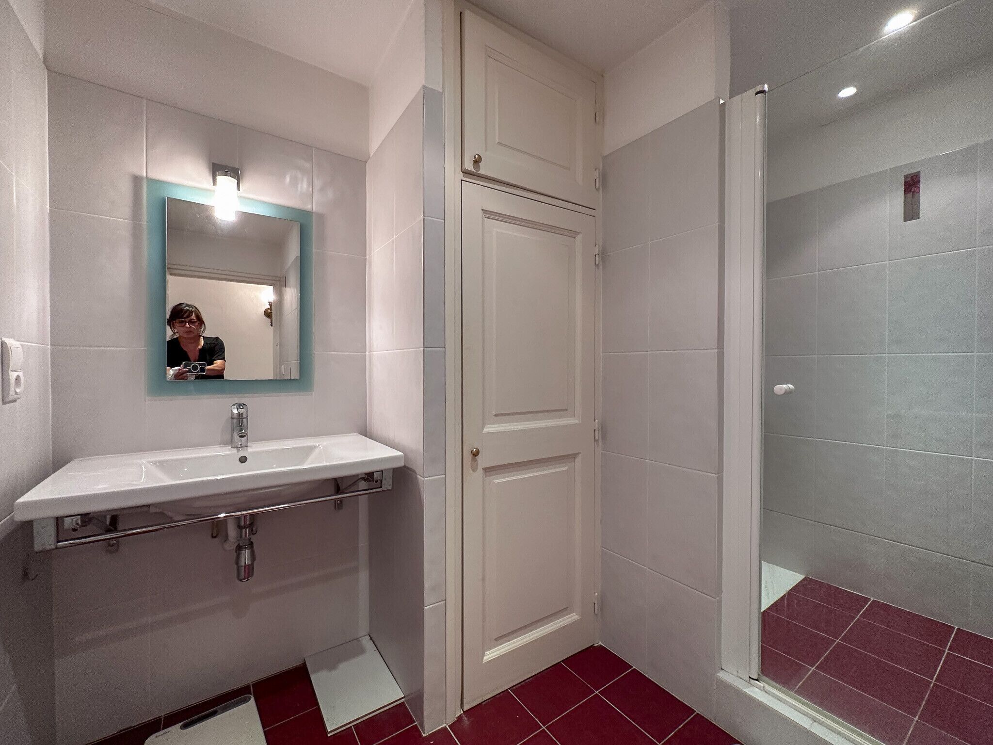 Une salle de bain avec un lavabo blanc, un miroir avec un cadre turquoise, une porte et un espace douche.